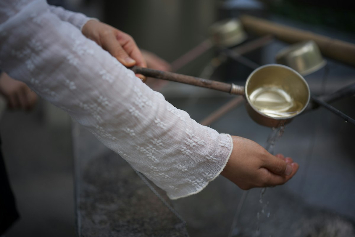 Du khách dùng gáo múc nước rửa tay tại temizuya trước khi vào đền