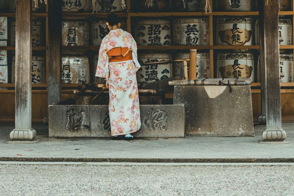 Cô gái mặc kimono đứng trước những thùng rượu sake tại đền Thần đạo