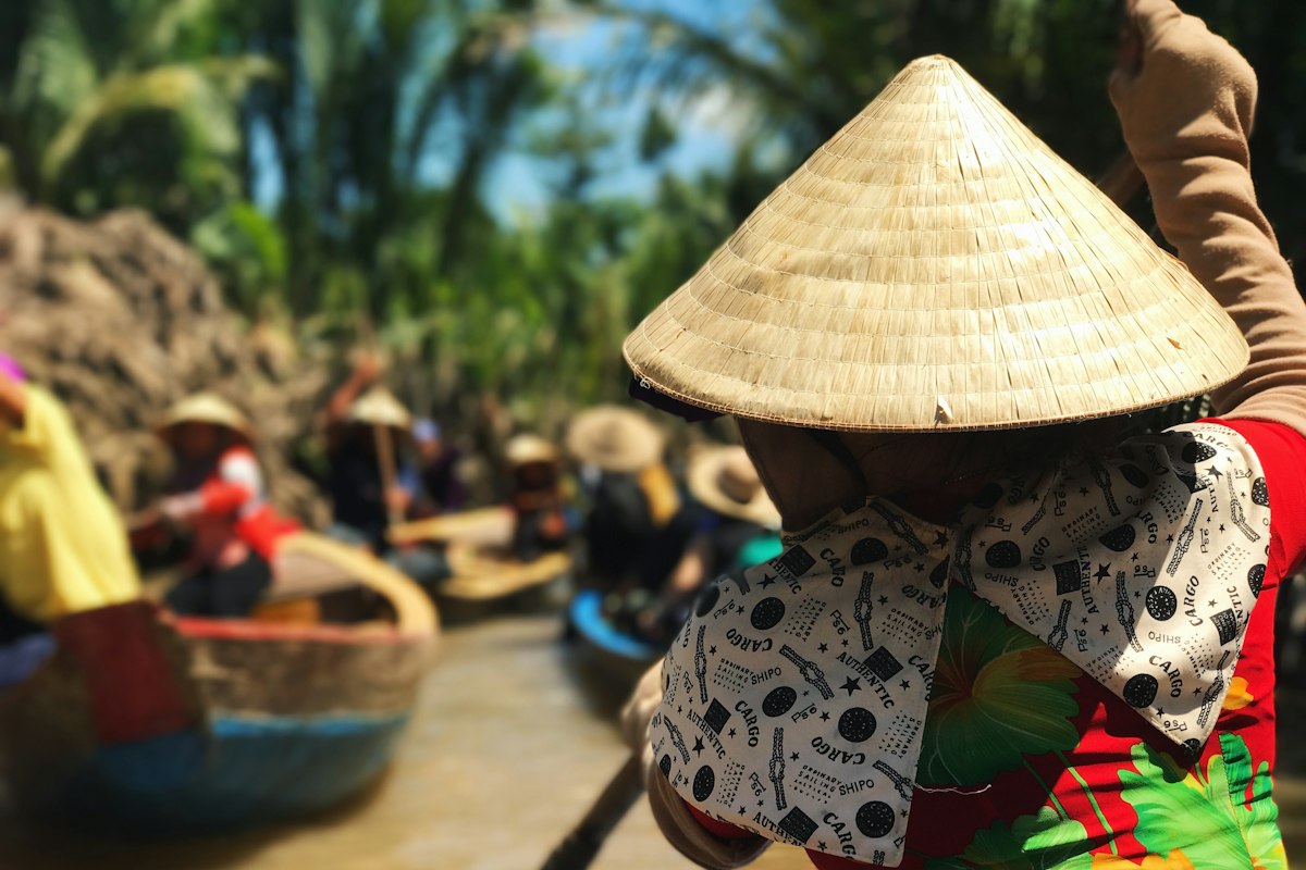 Du khách đội nón lá đi xuồng trên sông miền Tây