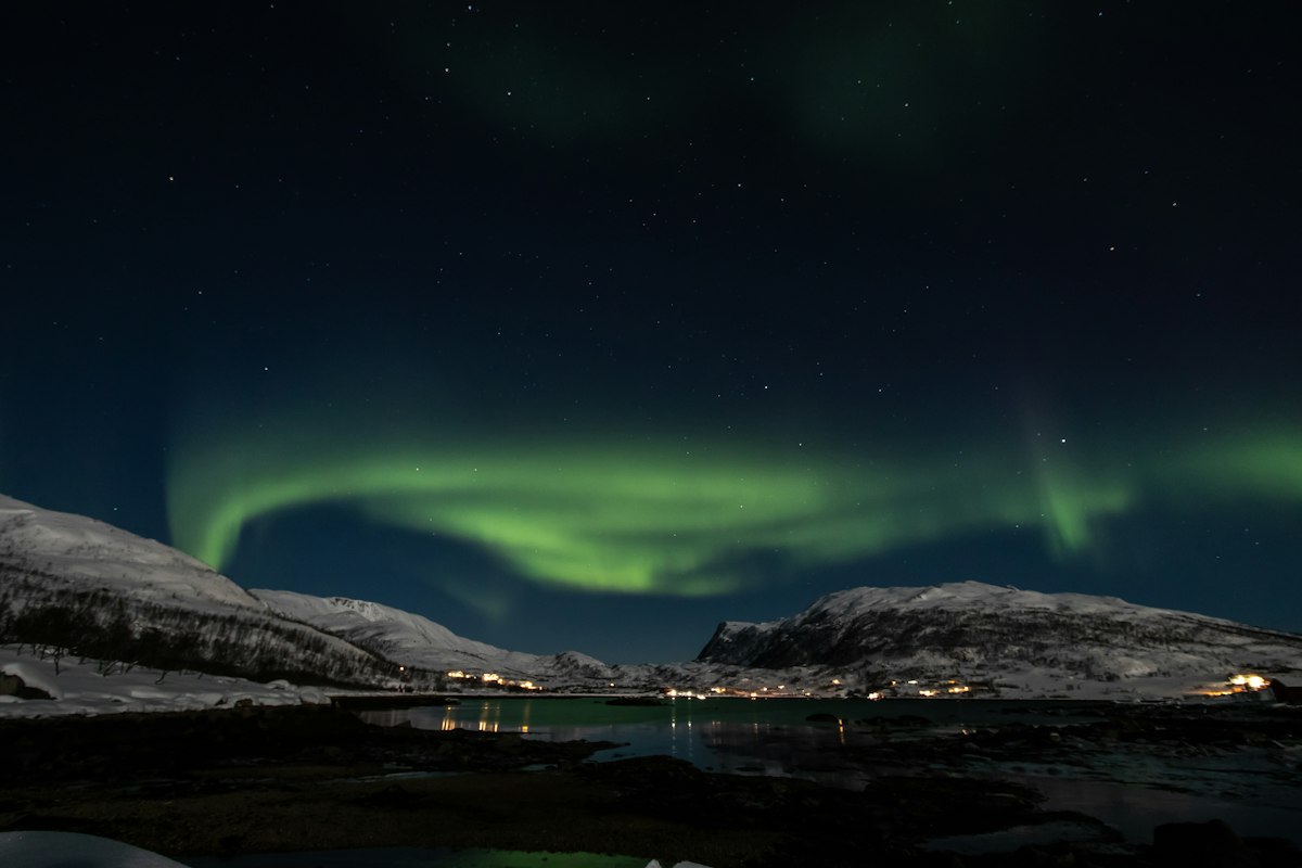 Cực quang xanh trên núi tuyết và vịnh biển Tromsø